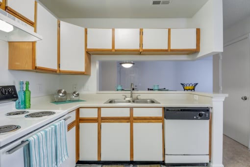 The three bedroom kitchen has white cabinets with tan trim, white appliances, formica countertops, and a double basin sink with gooseneck faucet. The breakfast bar has a place setting of fiesta ware for two.