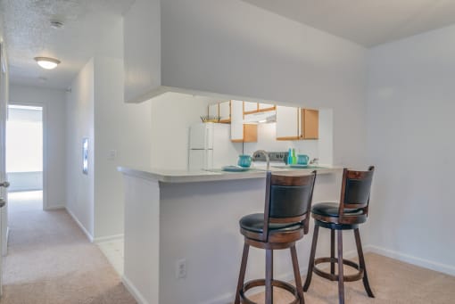 The three bedroom kitchen features a breakfast bar, white cabinets with tan trim, and white appliances. This mini model has two barstools at the breakfast bar.