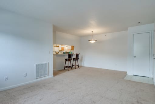 The living and dining room has carpet with linoleum flooring in the entry. There is breakfast bar that opens to the kitchen. This mini model is furnished with two barstools positioned at the breakfast bar.