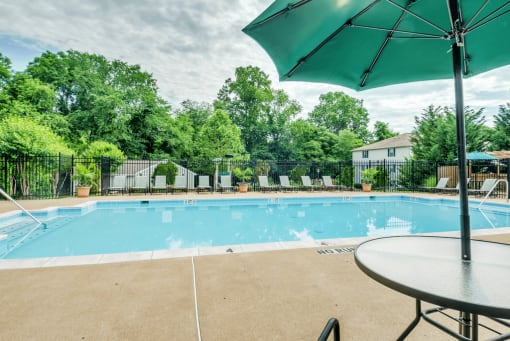 Swimming pool with lounge seating, shaded picnic seating, surrounded by native landscaping, and apartment building exterior in the background