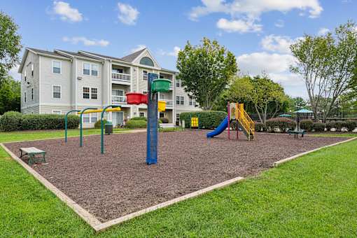 A playground with a slide, swings, and a seesaw in front of a building.