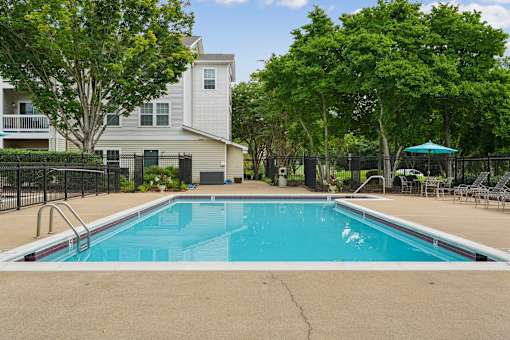 A swimming pool in a residential area with a house and trees in the background.