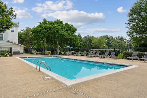 A swimming pool surrounded by trees and chairs.