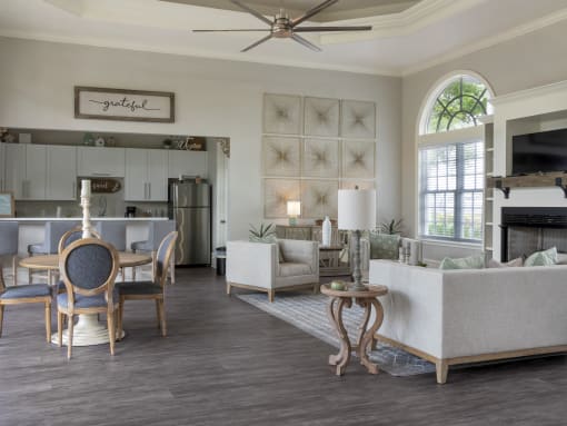 Clubhouse lounge with couches, décor, tables and chairs. Clubhouse kitchen with stainless steel appliances, white cabinets, and a breakfast bar with 4 barstools.