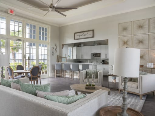 Clubhouse lounge with couches, décor, tables and chairs with clubhouse kitchen in the background