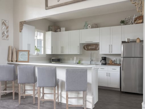 Clubhouse kitchen with stainless steel appliances, white cabinets, and a breakfast bar with 4 barstools.