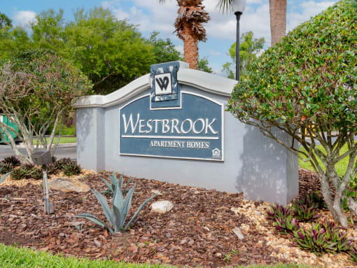Property Sign with landscaping shrubbery underneath it and trees in the back ground