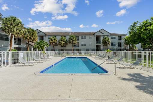 A swimming pool in front of a building with palm trees.