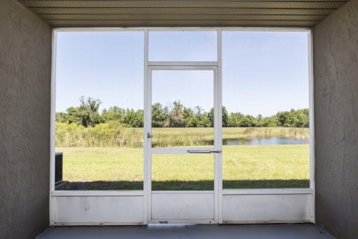 a view of a field and a pond through a glass door