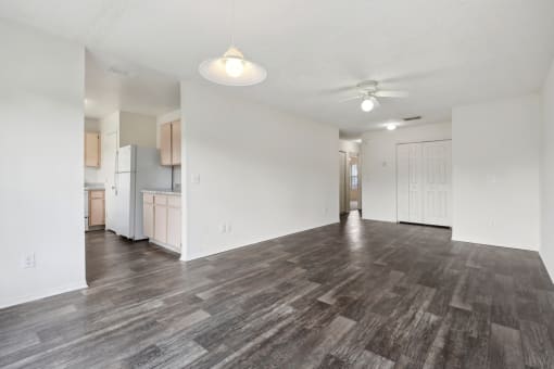 the living room and kitchen of an apartment with wood flooring and a ceiling fan
