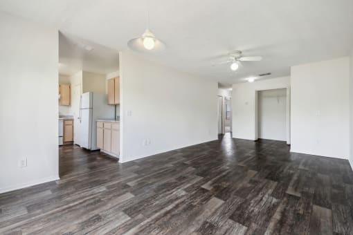 the living room and kitchen of an apartment with wood flooring and a ceiling fan