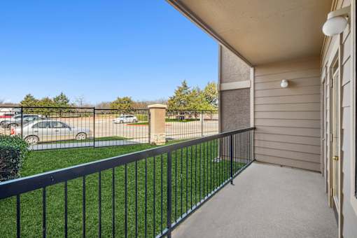 A balcony with a black railing overlooking a parking lot.