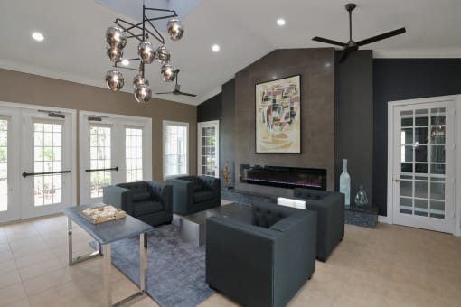 The Resident Lounge is a big room with a contemporary design. The far wall shows a large painting artwork above a fireplace. Four dark chairs are sat around a small table in front of french doors.