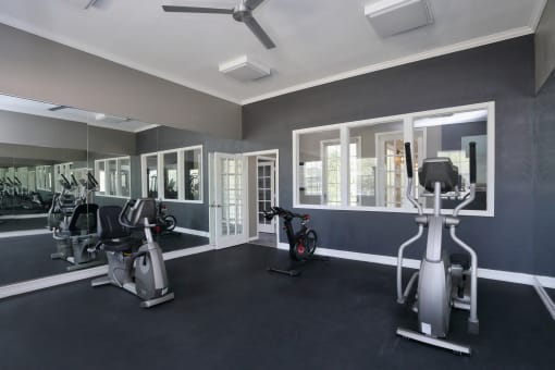 The Cardio Fitness Studio is a large room painted in dark colors with a full mirrored wall. Two silver cardio equipment pieces are placed around the room with large windows facing the hallway.