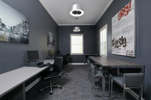 The Computer Lab is a long room painted in dark colors with artwork mounted on walls throughout. The left wall has a long counter with the computers placed on top. A small table and chairs are on the right wall.