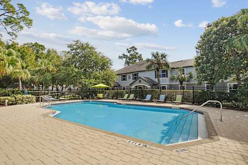 A pool surrounded by trees and a house in the background.