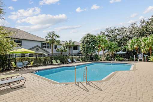 A swimming pool surrounded by a brick patio and lounge chairs.