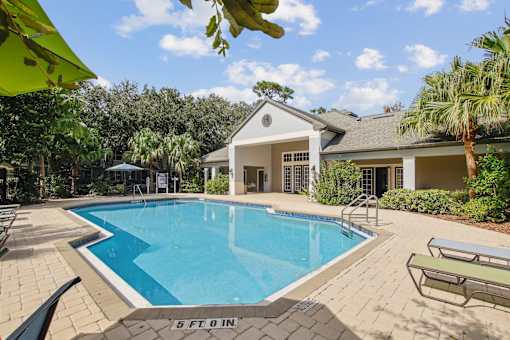A pool with the depth of 5 feet is surrounded by a house and trees.