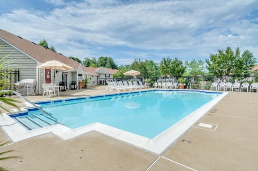 Swimming pool with picnic tables and umbrella. Lounge chairs and mature tress in the background .