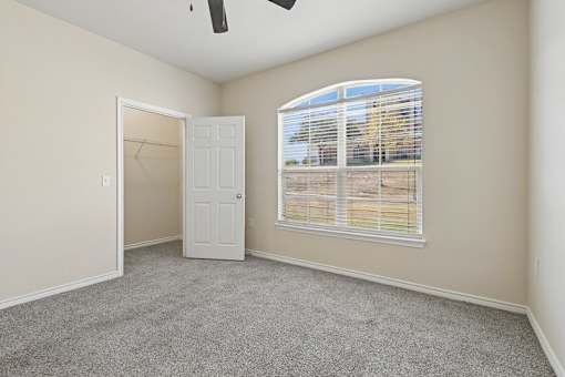 A bedroom with a ceiling fan, a door, and a window with blinds.