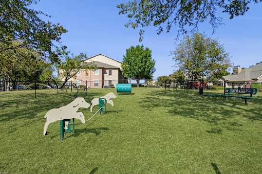 A dog park with a green lawn agility equipment
