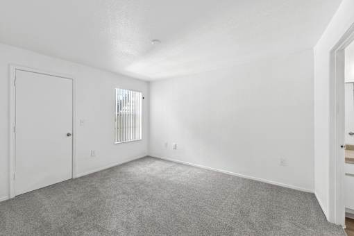 A white room with a carpeted floor and a window with blinds.
