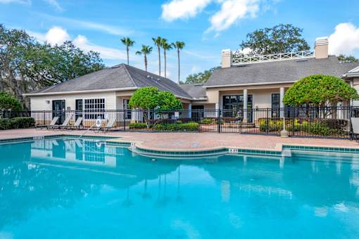 Leasing Office Exterior with Swimming Pool and Sun Deck with Lounge Chairs Near Treeline