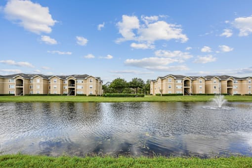 a pond with a fountain in front of a row of apartment buildings