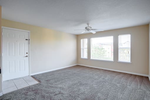 an empty room with a ceiling fan and three windows