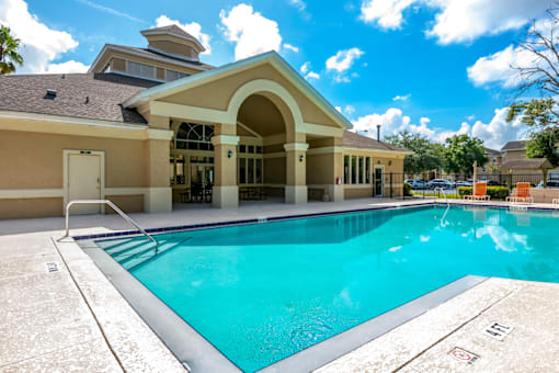 a swimming pool with a tanning deck and clubhouse in the background