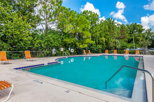 a swimming pool with orange chairs and trees in the background