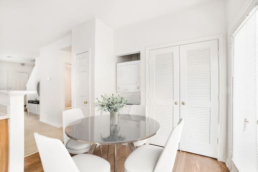 a dining room with white chairs and a glass table with a vase of flowers on it