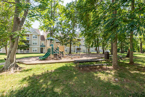 a park with a playground and trees in front of an apartment building
