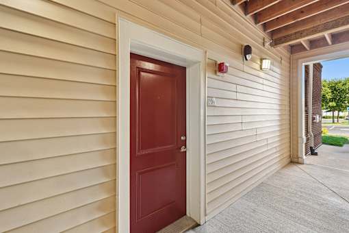 A red door is on the left side of a beige building.