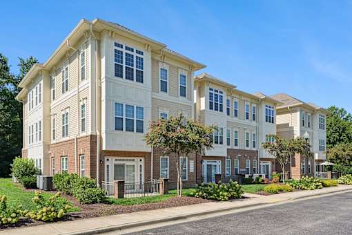A row of townhouses with a sidewalk and greenery in front.