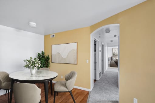 Virtually staged dining area dining table and chairs, wall art, wooden floor and entrance to hallway with tan accent wall