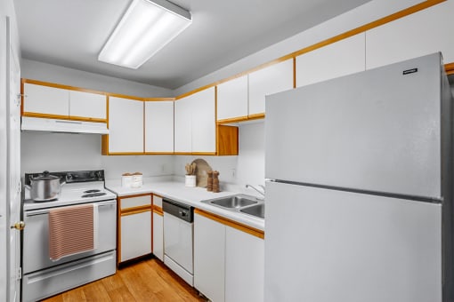 Virtually staged kitchen with pot on stove, white appliances, white cabinets, and wooden floors