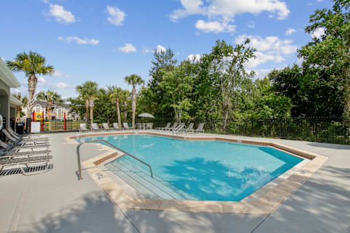 A large outdoor swimming pool surrounded by trees and lounge chairs.