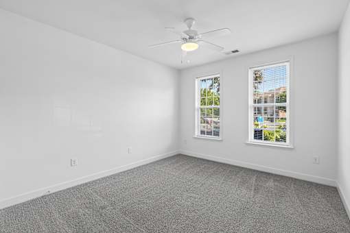A room with a ceiling fan and two windows.
