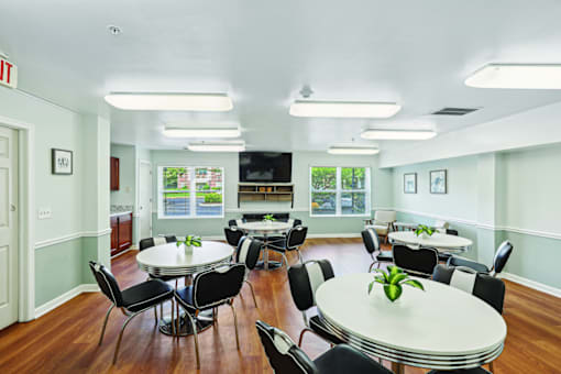 A white table with a green plant on it is surrounded by black chairs in a room with a white ceiling and a door with a red exit sign above it.
