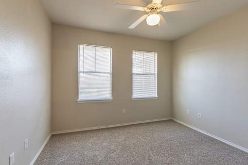 A room with a ceiling fan and two windows.