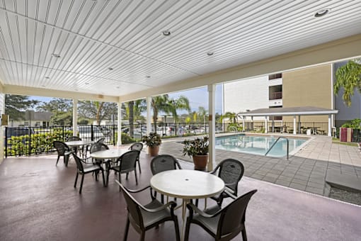 a patio with tables and chairs and a pool in the background