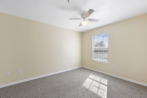 an empty bedroom with a ceiling fan and a window