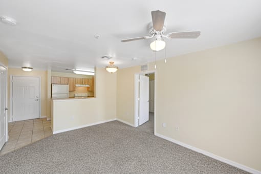 a living room with a ceiling fan and a kitchen in the background