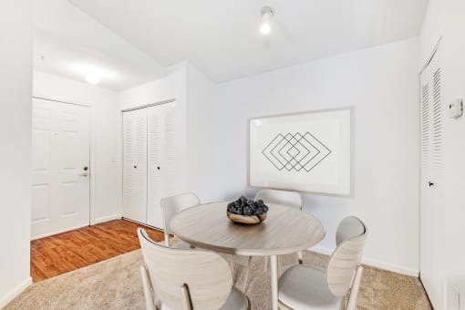 Vacant apartment entry area with closet and a carpeted dining area. Staged with a dining table and chairs and art on the wall.
