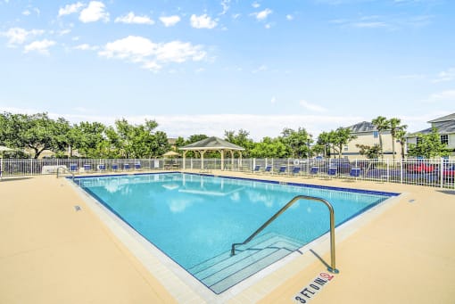 Swimming pool with lounge seating surrounded by native landscape and grill pavilion in background