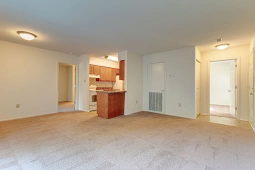 an empty living room with a kitchen in the background
