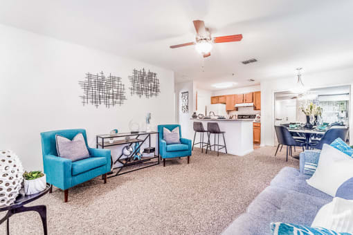 Modeled living room with carpet and ceiling fan open to a dining area and breakfast bar.