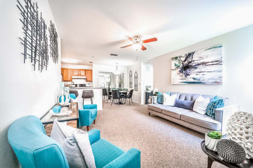 Modeled living room with carpet and ceiling fan open to a dining area and breakfast bar.