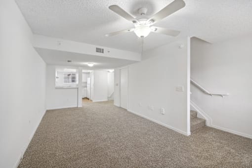 the living room of an apartment with carpet and a ceiling fan